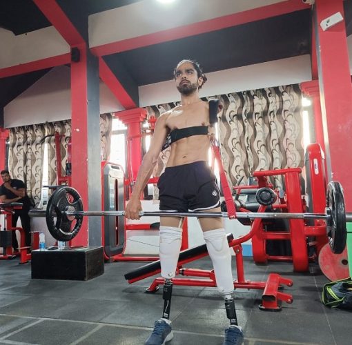 The TAF Co-Founder standing in the gym, weightlifting a heavy barbell using his prosthetics having a determined look on his face
