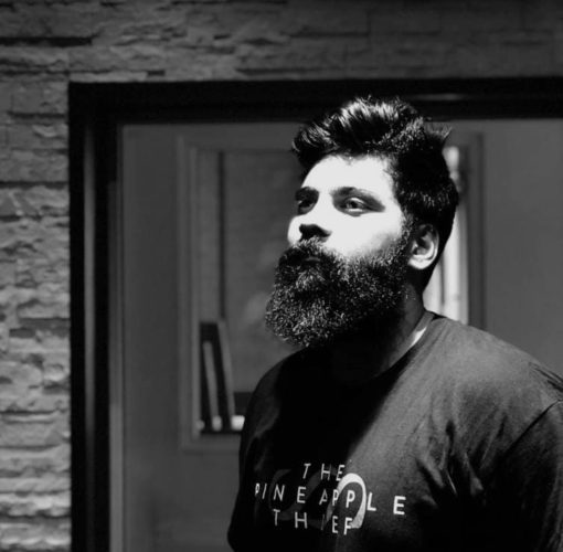 black and white image of man in front of a door wearing a t-shirt that reads "the pineapple thief" with a bear, moustache, and straight short hair