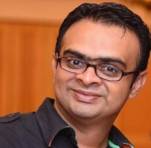 man with specs, wearing a purple shirt, black hair, smiling at the camera