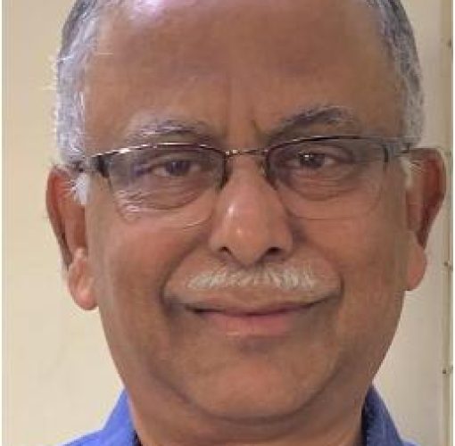 man with white hair and a moustache, wearing specs and a blue shirt, smiling at the camera